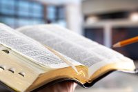 A man holds a Bible with a pencil, against the background of the living room.