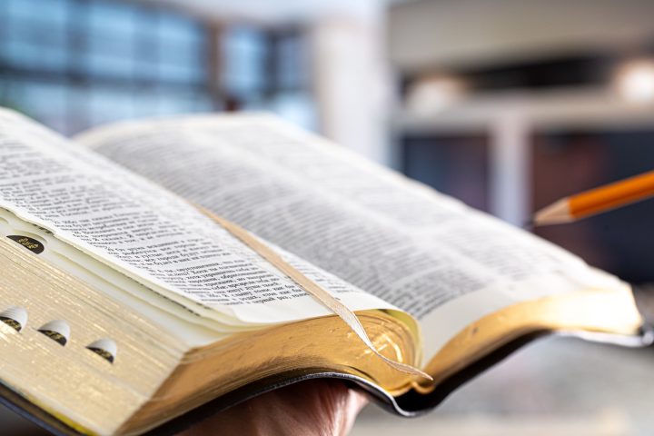 A man holds a Bible with a pencil, against the background of the living room.